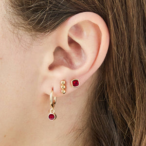 Close-up of an ear wearing gold earrings with red gemstones.