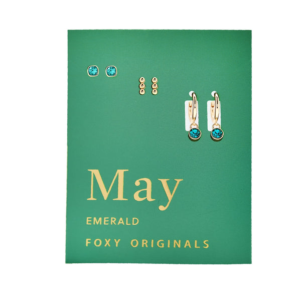 Jewelry set with 'May' and 'Emerald' text on a green card, featuring gold and gemstone earrings.